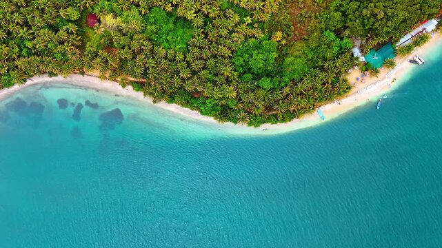 Overhead view of a palm covered island tip in turquoise sea, Panama. Top down perspective of sandy shore, coral patches and moored boats near green canopy.