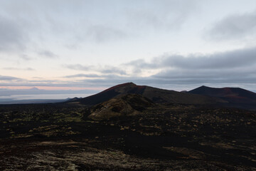 Fototapeta premium Wide view of Tolbachinsky Dol volcanic plateau with dark cinder cones, black lava fields and sparse moss under dramatic clouds, Kamchatka Krai, Russia