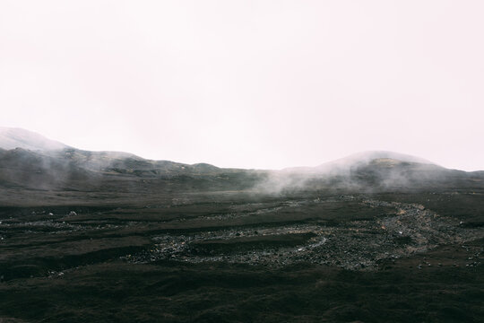 Wide view of dark volcanic lava fields with drifting fog and low hills in Tolbachinsky Dol, Kamchatka Krai, Russia, dramatic wilderness scenery under overcast sky