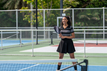 Obraz premium Young woman playing pickleball match on outdoor court. Athletic female player holding paddle racket waiting for ball during padel tennis game training session