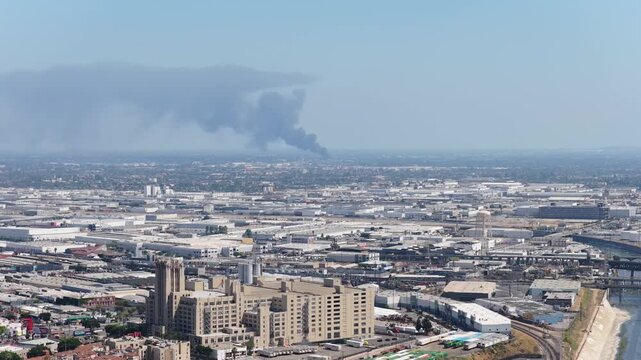Urban expanse of Los Angeles showing LAC plus USC Medical Center with large column of black smoke rising from a building fire, polluting cityscape