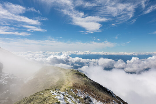 Scenic view from Avachinsky Volcano ridge above a sea of clouds under bright blue sky, Kamchatka Krai, Russia, showcasing remote wilderness and volcanic terrain