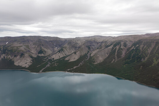 Wide aerial landscape of Ksudach volcano caldera with turquoise crater lake, steep volcanic slopes and tundra under overcast sky, Kamchatka Krai, Russia