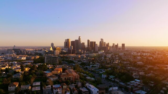 Aerial view of Los Angeles downtown skyline captured at sunset. Traffic congestion visible on highways. Skyscrapers and office towers dominate the urban landscape.