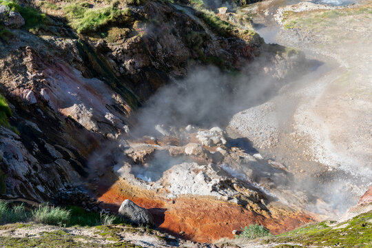 Geothermal steam rises from hot springs and fumaroles among colorful mineral deposits and rocks in Valley of Geysers, Kamchatka Krai, Russia, volcanic landscape