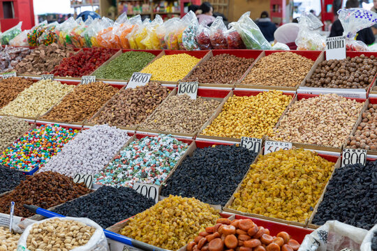 Assortment of dried fruits, nuts, seeds and colorful sweets displayed in open boxes at a busy market stall in Osh Bazaar, Bishkek, Kyrgyzstan