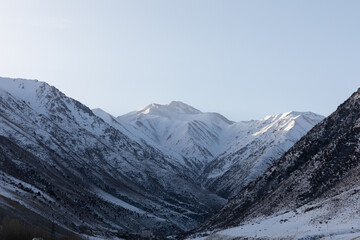 Fototapeta premium Wide view of snow-covered mountains and deep valley in Chunkurchak Valley, Chuy Region, Kyrgyzstan, with rugged slopes, cold winter light and clear blue sky