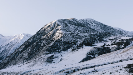 Fototapeta premium Snow-covered mountain ridge and scattered conifer forest in Chunkurchak Valley, Chuy Region, Kyrgyzstan, clear winter day with calm wilderness scenery