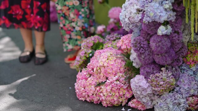 Colorful flower arrangement with hydrangeas and alliums decorating an urban street. People wearing floral dresses are walking in the background
