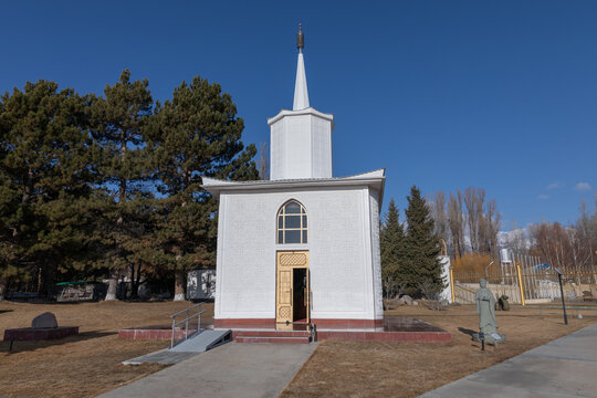 Cholpon-Ata, Kyrgyzstan - February 28, 2025: Front view of a small white chapel with a tall spire at the Rukh Ordo cultural complex in Cholpon-Ata, Issyk-Kul Region, Kyrgyzstan, on a sunny day