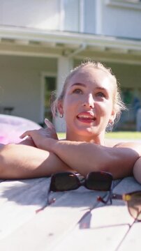 Vertical video: Leaning woman in swimsuit laughing after friend speaking at pool deck, sunglasses