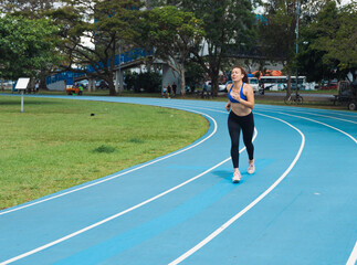 Fototapeta premium Woman running on blue athletic track during workout