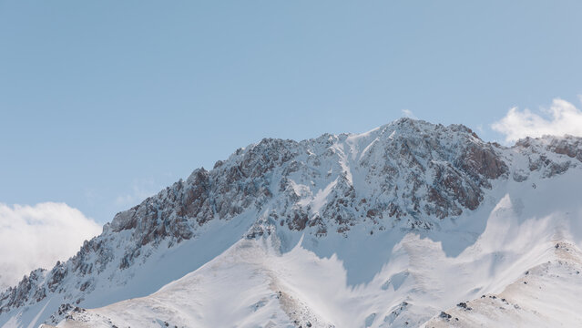 Winter mountain landscape with rugged snow-covered peaks and rocky ridge under clear blue sky in Alay Valley, Osh Region, Kyrgyzstan, Central Asia travel scenery