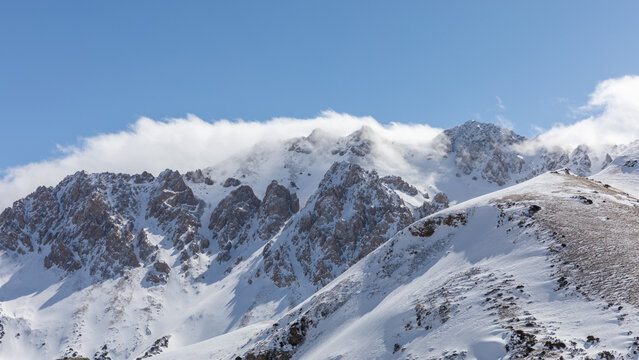 Wide view of snow-covered mountains with jagged rocky peaks and drifting clouds on a clear day in Alay Valley, Osh Region, Kyrgyzstan, Central Asia