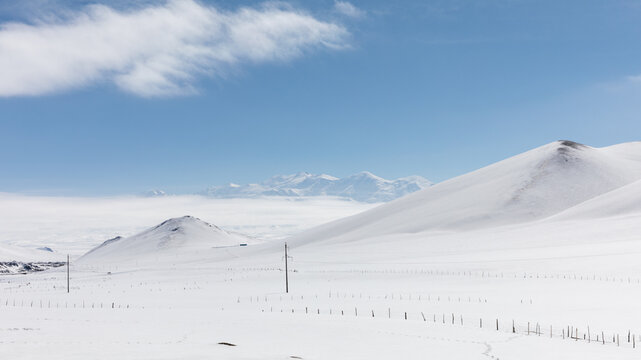Wide winter landscape in the Alay Valley with smooth snow-covered hills, distant mountain range and blue sky, remote highland scenery in Osh Region, Kyrgyzstan
