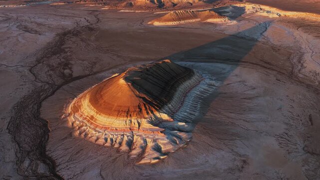 Aerial view of Mount Bokty featuring colorful layered strata and long shadows in the arid desert landscape of Karakiya District, Mangystau Region, Kazakhstan.