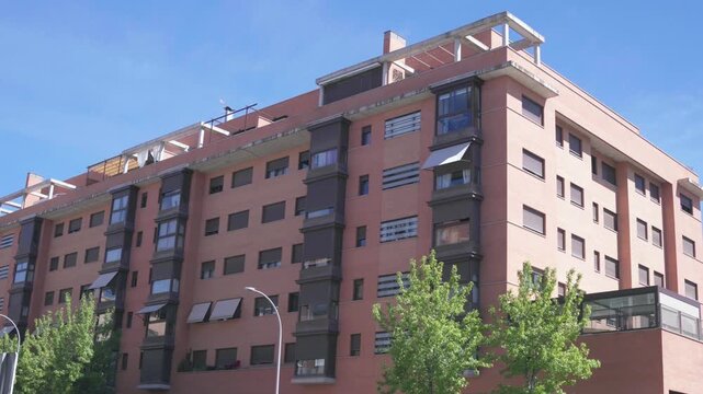 Modern residential apartment building featuring terracotta facade, balconies and contemporary urban housing architecture. Exterior view of multi-story residential development on a sunny day.