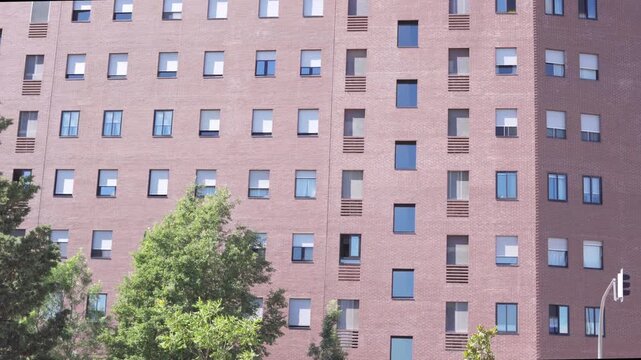 Modern red brick residential apartment building facade with repetitive window pattern and contemporary urban housing design. Exterior architectural view on a sunny day.