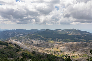 Fototapeta premium Wide panoramic view of rocky mountains, forests and valleys under dramatic cloudy sky in Lovcen National Park, Montenegro, a scenic nature travel destination