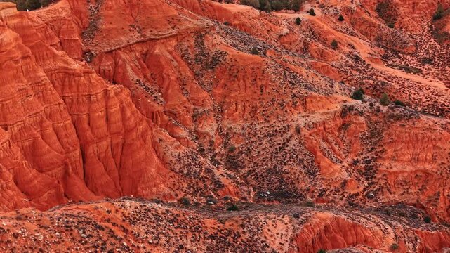 Eroded red clay hillside with layered sediment, Spain. Close up texture of ridges, gullies and sparse scrub on orange terrain.