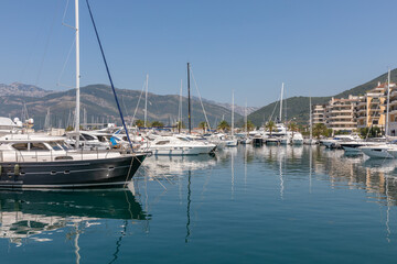 Fototapeta premium Tivat, Montenegro - August 11, 2025: Sunny view of Porto Montenegro marina with luxury yachts, sailboats and waterfront apartments, reflected in calm water, Tivat, Bay of Kotor, Montenegro