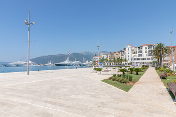 Fototapeta premium Tivat, Montenegro - August 11, 2025: Sunny waterfront view of Porto Montenegro marina with luxury yachts, modern promenade, palm trees and coastal buildings in Tivat, Montenegro, on a clear summer day