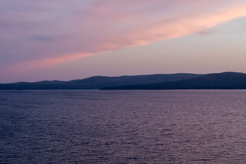 Fototapeta premium Serene evening landscape of Lake Turgoyak with gentle ripples, distant Ural Mountains ridge and soft pink clouds at dusk, tranquil nature background with copy space
