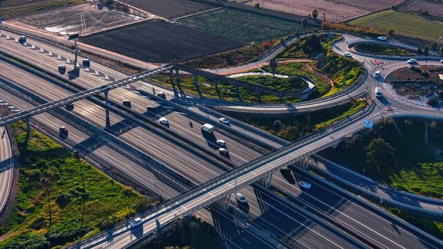 Aerial view of a multi lane highway interchange in Valencia, Spain. Drone perspective of asphalt roads, overpass bridge, green grass fields and moving cars.