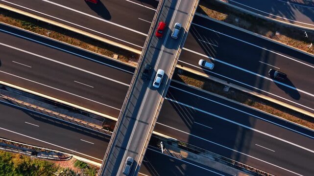 Vehicles crossing a road bridge over a highway in Spain. Close overhead view of cars on asphalt lanes casting long shadows on the freeway below.