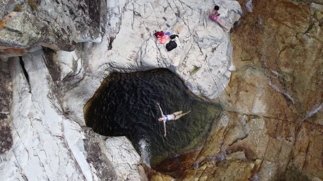 Aerial view of a woman floating with arms outstretched in a crystal-clear natural pool at Capivara Waterfall, Serra da Canastra, Brazil, surrounded by pristine nature and tropical landscapes.
