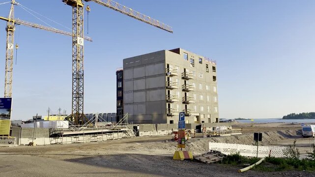 Zoom in Grey Concrete Apartment Building Construction Site with Crane Against Blue Summer Sky