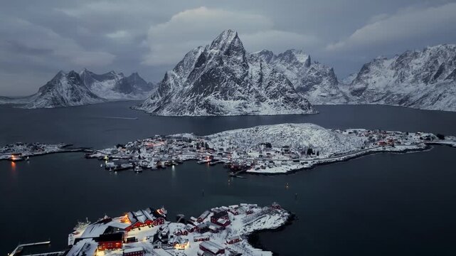 Aerial dusk view of snowy coastal fishing village on rocky islets
