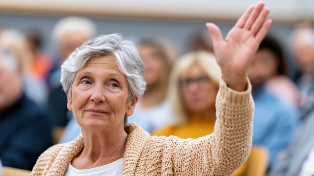 Elderly woman with gray hair raises her hand during a public meeting