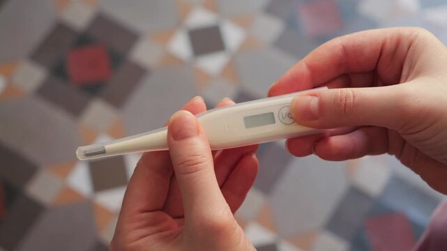 Hand taking a digital thermometer out of a plastic case and pressing the button to turn it on. Close-up of activating a medical device for temperature measurement. High quality 4k footage
