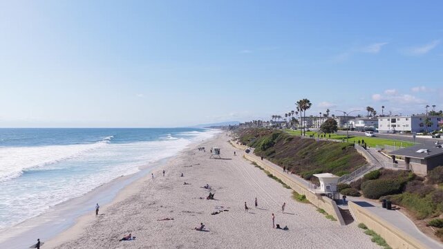 Carlsbad State Beach featuring vibrant green bluffs and people walking along ocean coastline and sandy shoreline with gentle breaking waves on sunny day in California