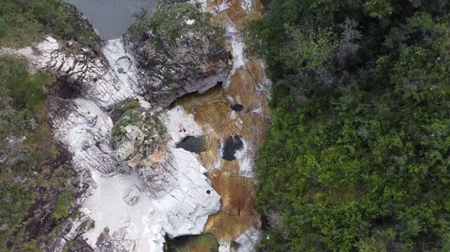 Aerial view of a man enjoying the natural pools at Capivara Waterfall, Serra da Canastra, Brazil, surrounded by crystal-clear water, rocky landscapes, pristine nature, and a scenic tropical setting.