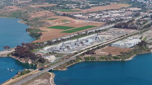 Scenic aerial of Encina Power Station and Agua Hedionda Lagoon in Carlsbad California with Interstate 5 traffic and agricultural fields showing urban development