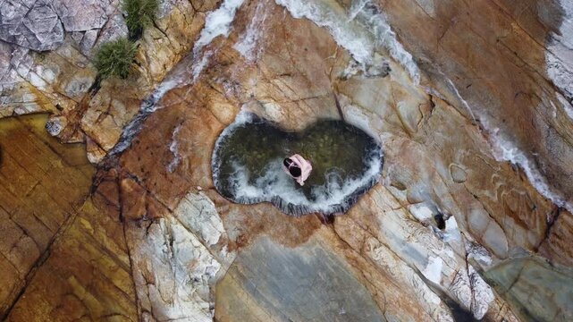Couple embracing and kissing in the heart-shaped natural pool at Capivara Waterfall, Serra da Canastra, Brazil, filmed by drone above crystal-clear waters and surrounded by pristine nature.