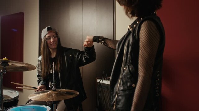 Caucasian female teenager playing drums in music studio, then giving fist bump to bandmate. Footage is ideal for youth culture advertisements, music school promotions, or lifestyle brand marketing