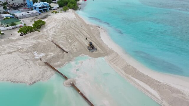 Aerial view of land reclamation and beach construction with machinery and pipes on the shore of Gulhi, Kaafu Atoll, Maldives.