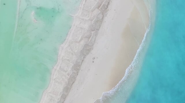 Aerial view of a pristine white sandbar meeting crystal clear turquoise and emerald waters with sand patterns on the shore in Gulhi, Kaafu Atoll, Maldives.