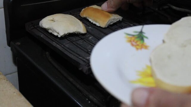 Un hombre con su mano toma las rodajas de pan y las coloca sobre el tostador r&uacute;stico de la cocina de campo para hacer las tostadas para el desayuno