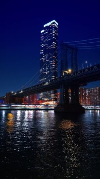 Night view of a bridge and a skyscraper, New York City, New York. Low angle vertical shot of illuminated suspension cables next to a tall glowing residential building.