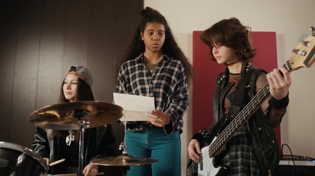 Diverse Caucasian and African American female teenagers rehearsing rock music in studio, reading lyrics and giving high fives. Video is ideal for youth lifestyle and music education ads
