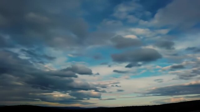 A dynamic time-lapse of vast, shifting cumulus and stratus clouds. A static ultra-wide video with a low horizon transitions from cool grey to vibrant cerulean sky with golden light. Symbolizing