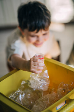 Child sorting plastic waste into a yellow recycling bin indoors