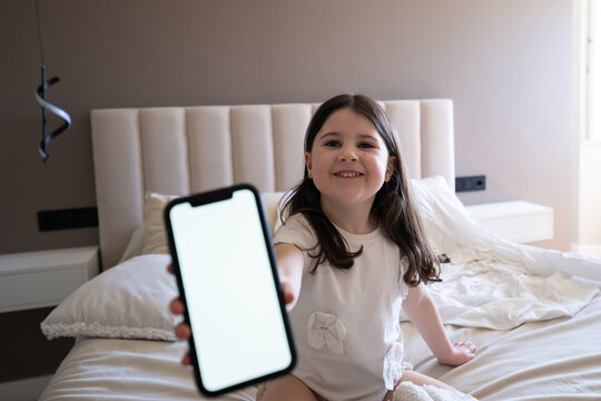 Smiling child holding smartphone with blank screen on bed at home