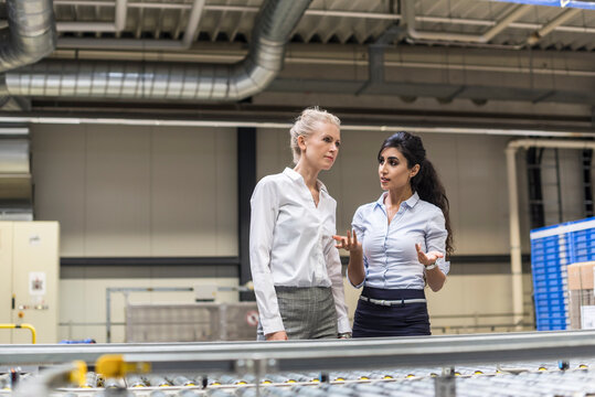 Two women discussing at conveyor belt in factory