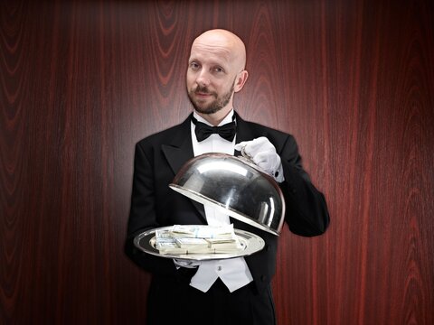 Butler presenting dollar banknotes on a silver tray indoors