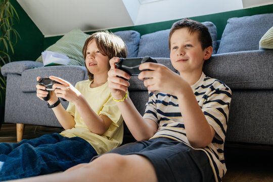Smiling brothers playing video game together indoors on floor